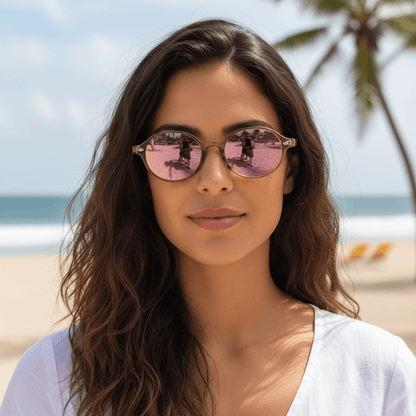 vista frontal de una mujer en la playa de cara ovalada usando gafas de sol polarizadas ovaladas color rose espejadas con lentes de color rosado espejado modelo Capri de Bonoboss. Anteojos ovalados retro de moda para hombre y mujer #color_rose