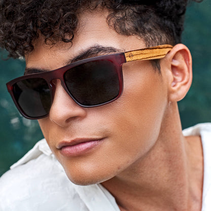 un modelo de pelo rulos en primer plano mirando en 45 grados hacia la izquierda usando anteojos de sol de color rojo en plastico reciclado con patas de madera natural #color-marco_wine